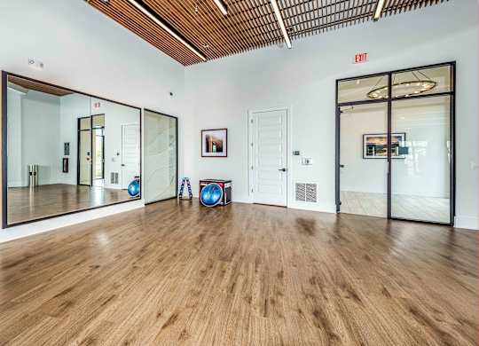 A room with wooden floors and a white wall with a red exit sign.