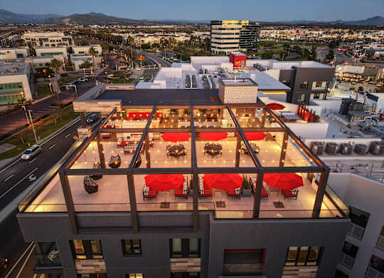 A rooftop restaurant with red umbrellas and tables.