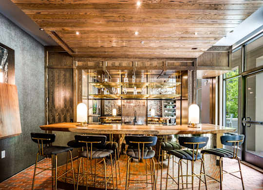 A wooden table with chairs and a bar area with bottles.