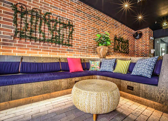 A room with a brick wall and a bench with cushions.