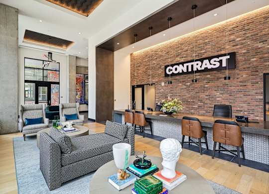 A living room with a grey couch and a brick wall with the word CONTRAST on it.