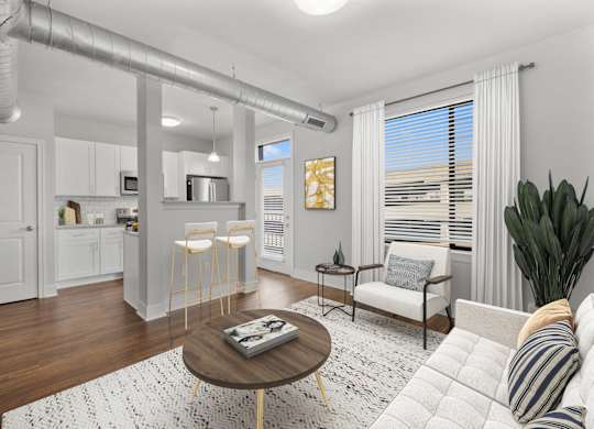 A modern living room with a white sofa, a wooden coffee table, and a kitchen area in the background at CityWay Apartments, Indianapolis, IN