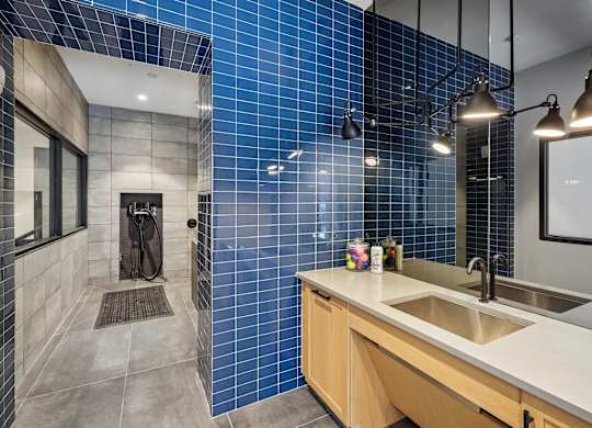 A modern bathroom with a blue tiled shower and a wooden vanity.