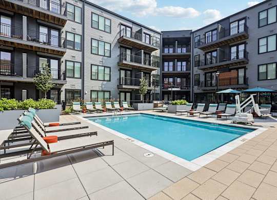 A swimming pool surrounded by lounge chairs and apartment buildings.