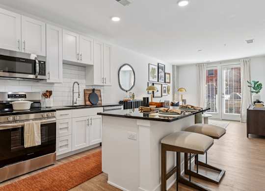 Modern kitchen at Contrast OTR in Cincinnati, OH featuring stainless steel appliances, white cabinetry, and a breakfast island with seating.