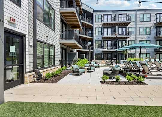 A patio area with chairs and umbrellas in front of apartment buildings.