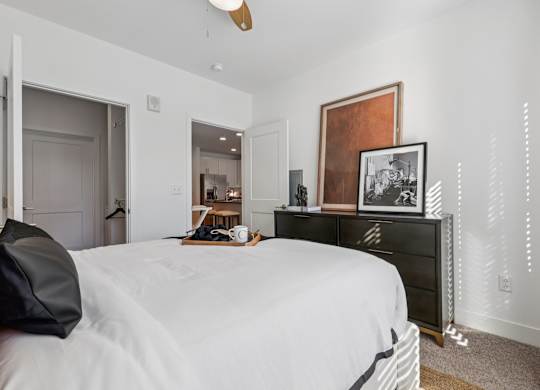Cozy bedroom at Contrast OTR apartments in Over-the-Rhine, Cincinnati showcasing textured artwork, modern dresser, and warm sunlight.