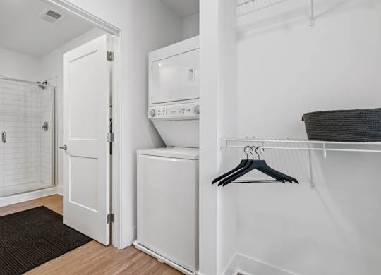 In-home laundry at Contrast OTR in Cincinnati, OH with stacked washer and dryer near walk-in closet and modern bathroom.