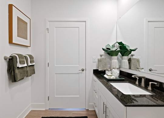 Modern bathroom at Contrast OTR in Cincinnati, OH featuring glass shower, granite countertops, and sleek white cabinetry.