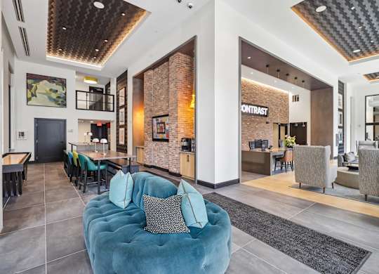 A blue couch with a pillow is in the middle of a room with a brick wall.