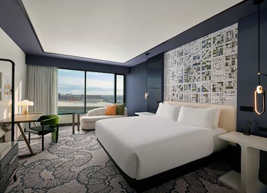 A modern hotel room with a large bed and a view of the city.