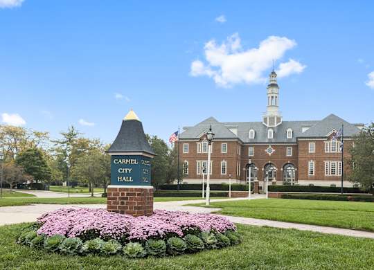 a large brick building with a sign in front of a lawn with flowers at Providence at Old Meridian Apartments , Carmel