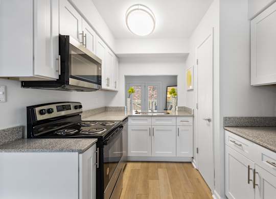 Modern galley kitchen at Monon Living in Broad Ripple featuring white shaker cabinets, granite countertops, and pass-through window with Monon Trail access nearby.