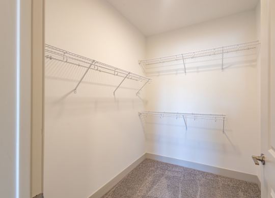 an empty closet with hanging rails and a door to a room with white walls