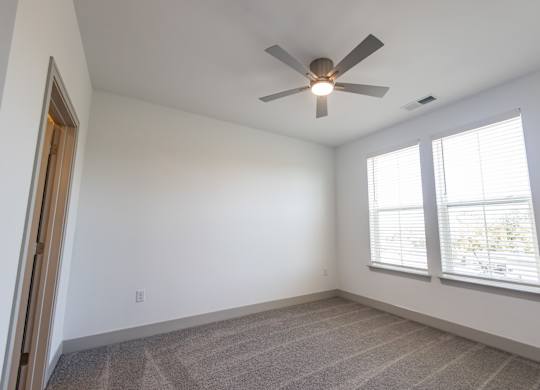 an empty room with a ceiling fan and two windows