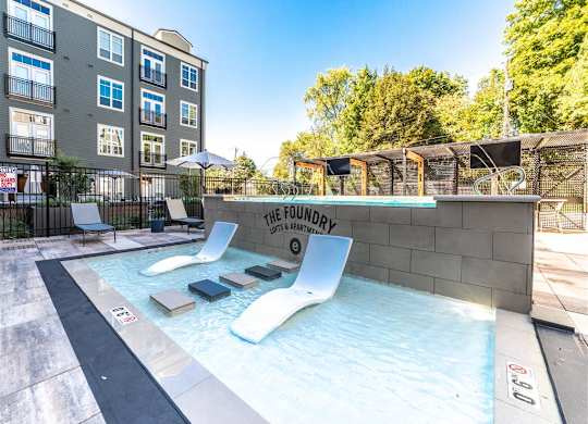 a pool with two lounge chairs in front of an apartment building at The Foundry, South Bend