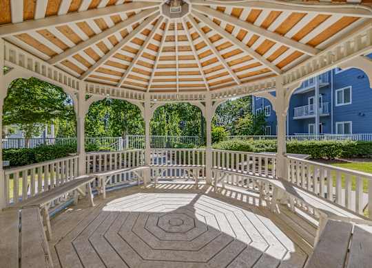 A gazebo with a white wooden frame and a peach colored roof is surrounded by a white railing.