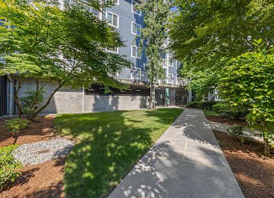 A concrete walkway leads through a landscaped area with trees and shrubs.
