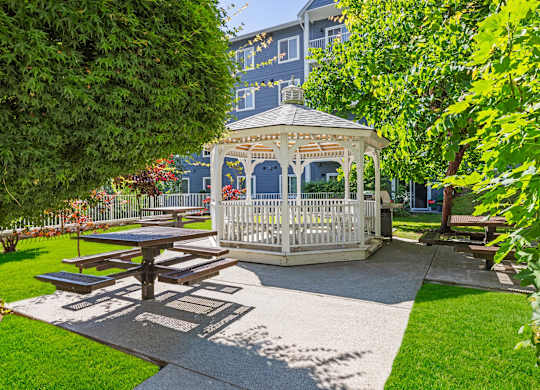 A gazebo is surrounded by a picnic table and a white picket fence.