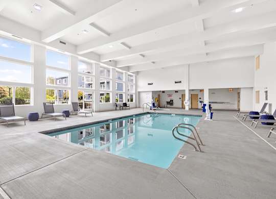 A large indoor swimming pool with lounge chairs and a view of the outside.