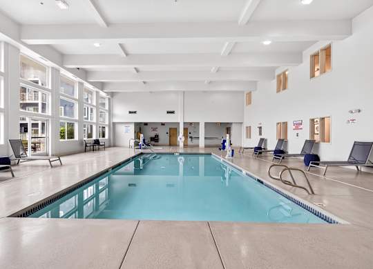 A large indoor swimming pool with lounge chairs and windows.