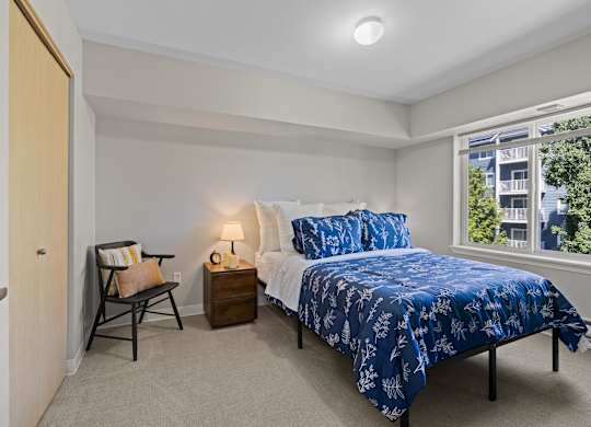 A bedroom with a bed, nightstand, and chair.