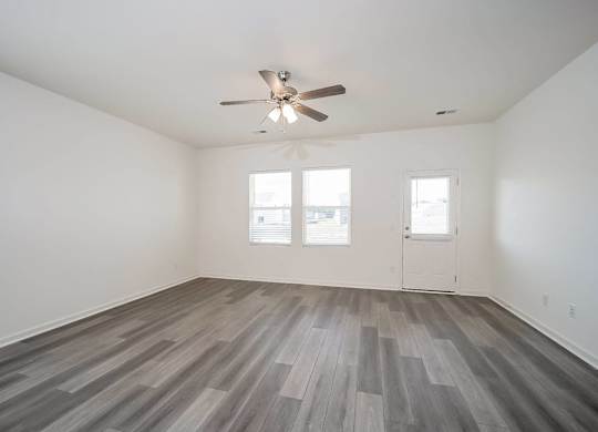 an empty living room with a ceiling fan and wood floors