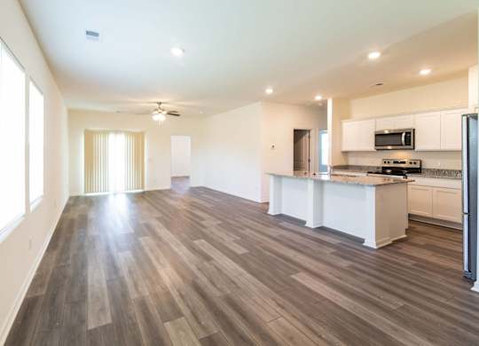 an empty living room and kitchen with wood flooring