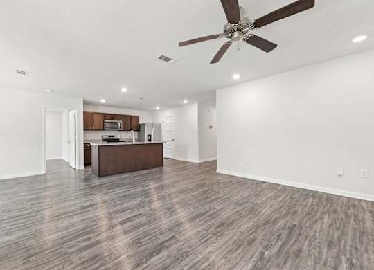 Open-concept kitchen and living area with gray wood-look flooring, brown cabinets, and a ceiling fan.