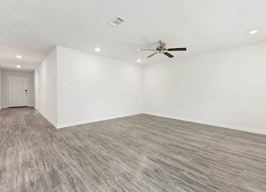 Empty room with gray wood-look flooring, white walls, ceiling fan, and recessed lighting.