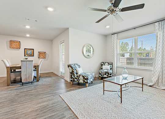 Interior view of a living and dining area with floral armchairs, glass coffee table, and wooden dining set.