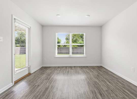 Empty room with gray wood-look flooring, white walls, a window with blinds, and a door leading outside.