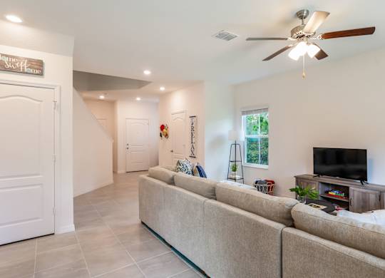 Bright, modern living room with a large sectional sofa, television, and tiled floors.
