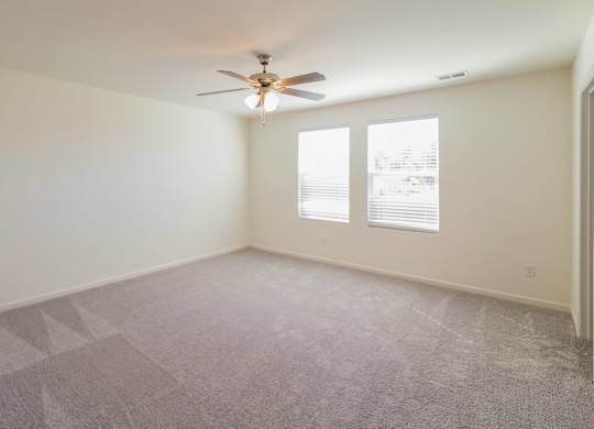 an empty living room with a ceiling fan and two windows
