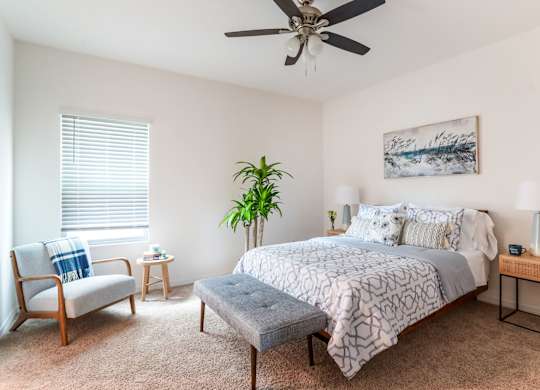 Bright, modern bedroom with geometric bedding, upholstered bench, armchair, and ceiling fan.