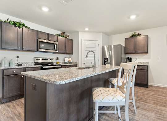 Modern kitchen with granite island, stainless steel appliances, and dark wood cabinets.