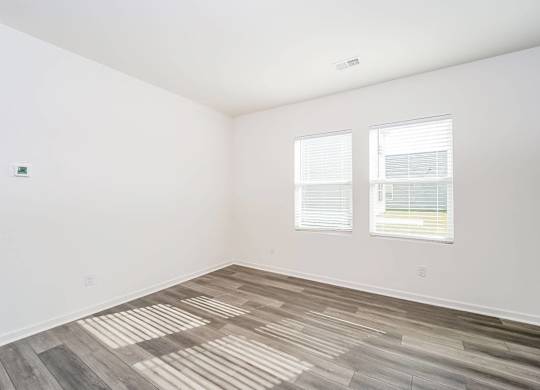 an empty room with wood flooring and two windows