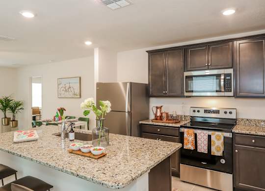 Modern kitchen with granite countertops, dark wood cabinets, stainless steel appliances, and island with seating.