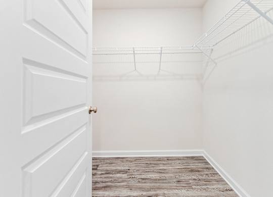 Empty walk-in closet with white walls, wood-look flooring, and wire shelving, viewed through an open door.