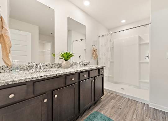 Modern bathroom with double vanity, granite countertop, dark wood cabinets, and white shower stall.