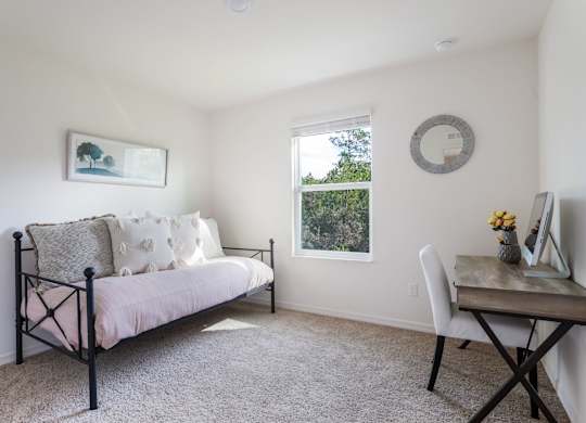Bright living room with daybed, desk, and window overlooking trees.