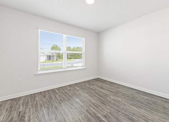 Empty room with gray wood flooring, white walls, ceiling fan, and window.