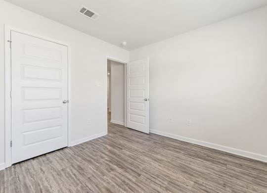 Empty white room with wood-look flooring, two paneled doors, and an open doorway.