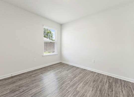 Empty room with gray wood-look flooring, white walls, and a window with blinds.
