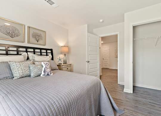 Bedroom with gray quilt, decorative pillows, open closet, and doorway to another room.