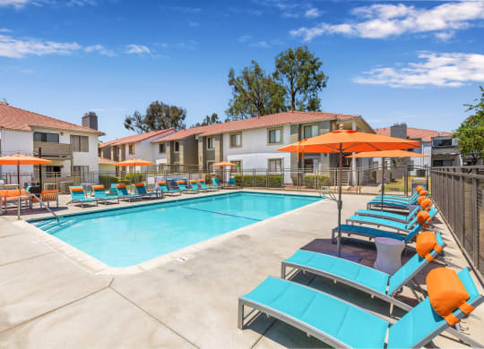 One-BR Apartments In Moreno Valley, CA - Gated Resort-Style Pool With Lounge Chairs, Tables, Chairs, Umbrellas, And BBQ Grill.