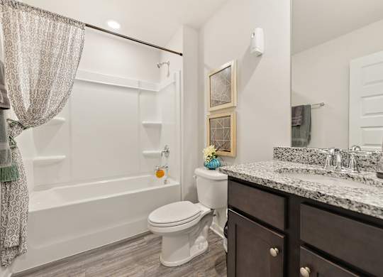 Modern bathroom with white tub and shower, toilet, and granite countertop vanity.