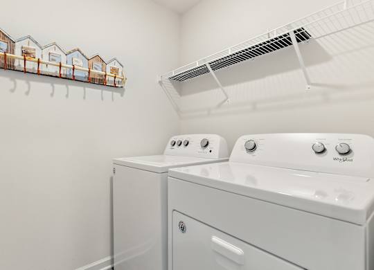 Laundry room with white Whirlpool washer and dryer, wire shelf, and beach hut-themed coat rack.