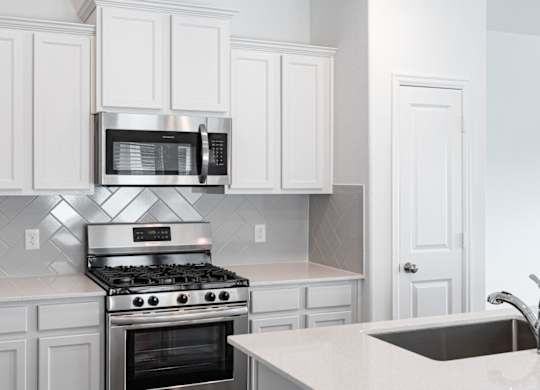 Houses in Humble, TX for Rent - Edgewater at the Lagoon - Kitchen with White Cabinets, Stainless Steel Appliances, Quartz Countertops, and Tile Backsplash