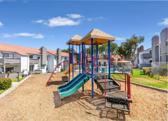 Apartments For Rent In Moreno Valley, CA - Sorelle Apartments - Playground with Slide Towers and View of Pool and Apartment Buildings.